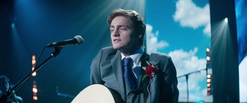 Movie still from “Clouds” (2020), directed by Justin Baldoni – A man in a suit and tie holding a microphone; Medium shot, Low angle