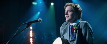 Movie still from “Clouds” (2020), directed by Justin Baldoni – A man in a suit and a microphone in front of a microphone stand; Medium shot, Over the shoulder angle