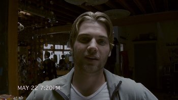 Movie still from “Cloverfield” (2008), directed by Matt Reeves – A young man with long blonde hair is smiling for the camera; Close Up shot, Low angle
