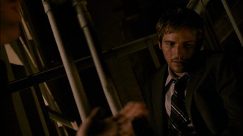 Movie still from “Cloverfield” (2008), directed by Matt Reeves – A man wearing a suit and tie standing in front of a metal fence; Close Up shot, Over the shoulder angle