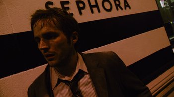 Movie still from “Cloverfield” (2008), directed by Matt Reeves – A man in a suit and tie standing in front of a sephora sign; Close Up shot, High angle