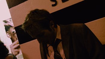 Movie still from “Cloverfield” (2008), directed by Matt Reeves – A man in a suit and tie leaning against a wall; Close Up shot, Low angle