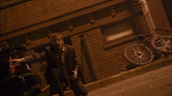 Movie still from “Cloverfield” (2008), directed by Matt Reeves – A man in a suit and tie sitting on the side of the street; Wide shot, Low angle
