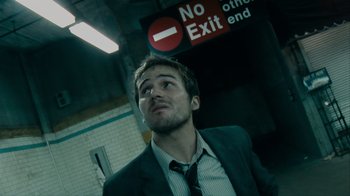 Movie still from “Cloverfield” (2008), directed by Matt Reeves – A man wearing a suit and tie in front of a no exit sign; Close Up shot, Low angle