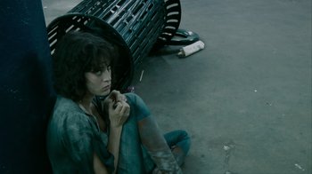 Movie still from “Cloverfield” (2008), directed by Matt Reeves – A woman sitting on the ground next to a metal bench; Medium shot, High angle
