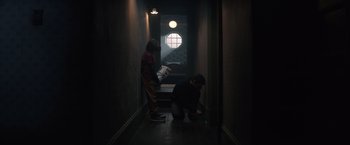 Movie still from “Cobweb” (2023), directed by Samuel Bodin – Two people in a dark hallway looking at a book; Wide shot, Low angle