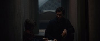 Movie still from “Cobweb” (2023), directed by Samuel Bodin – A man and a boy are looking at a book together; Medium shot, Over the shoulder angle