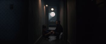 Movie still from “Cobweb” (2023), directed by Samuel Bodin – A man and a woman sitting on the floor in a dark room; Wide shot, High angle