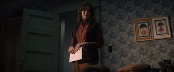 Movie still from “Cobweb” (2023), directed by Samuel Bodin – A woman standing in front of a wall holding a piece of paper; Medium shot, Over the shoulder angle