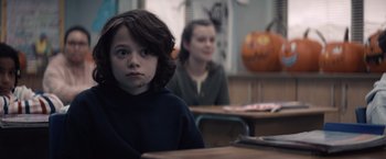Movie still from “Cobweb” (2023), directed by Samuel Bodin – A young boy sitting at a desk in front of a woman; Close Up shot, Over the shoulder angle