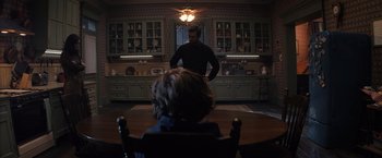 Movie still from “Cobweb” (2023), directed by Samuel Bodin – A man standing in front of a woman sitting at a dining room table; Wide shot, Over the shoulder angle