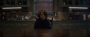 Movie still from “Cobweb” (2023), directed by Samuel Bodin – A boy sitting at a wooden table in a kitchen; Medium shot, Over the shoulder angle