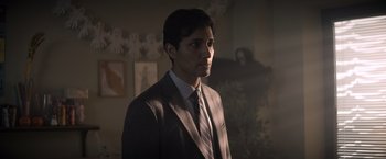 Movie still from “Cobweb” (2023), directed by Samuel Bodin – A man wearing a suit and tie standing in a room; Medium shot, Over the shoulder angle