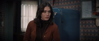 Movie still from “Cobweb” (2023), directed by Samuel Bodin – A woman in a brown jacket sitting in front of a blue suitcase; Close Up shot, Over the shoulder angle