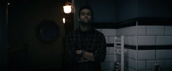 Movie still from “Cobweb” (2023), directed by Samuel Bodin – A man standing with his arms crossed in a dark room; Medium shot, Low angle