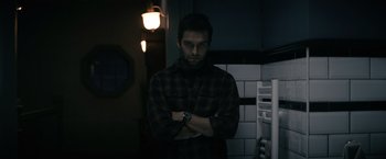 Movie still from “Cobweb” (2023), directed by Samuel Bodin – A man standing in a dark room with his arms crossed; Medium shot, Low angle