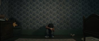 Movie still from “Cobweb” (2023), directed by Samuel Bodin – A person sitting on the ground in front of a wall; Wide shot, Overhead angle