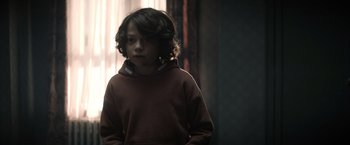 Movie still from “Cobweb” (2023), directed by Samuel Bodin – A young boy wearing a brown hoodie standing next to a window; Close Up shot, Over the shoulder angle