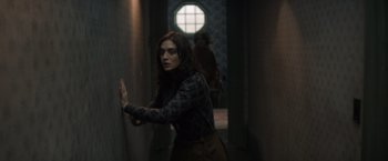 Movie still from “Cobweb” (2023), directed by Samuel Bodin – A woman standing in a dark hallway holding her hand up to the wall; Medium shot, Over the shoulder angle