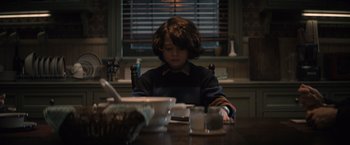 Movie still from “Cobweb” (2023), directed by Samuel Bodin – A boy sitting at a dining room table looking at a computer; Medium shot, High angle