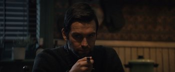 Movie still from “Cobweb” (2023), directed by Samuel Bodin – A man sitting in front of a wall holding a cell phone; Close Up shot, Over the shoulder angle