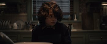 Movie still from “Cobweb” (2023), directed by Samuel Bodin – A young boy sitting at a table in front of a window; Close Up shot, Over the shoulder angle