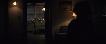 Movie still from “Cobweb” (2023), directed by Samuel Bodin – A person sitting on a chair in a dark room; Wide shot, Over the shoulder angle