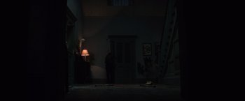 Movie still from “Cobweb” (2023), directed by Samuel Bodin – A person standing in a dark room with a lamp; Extreme Wide shot, High angle