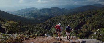 Movie still from “Cocaine Bear” (2023), directed by Elizabeth Banks – A couple of people that are standing on top of a hill; Extreme Wide shot, Low angle
