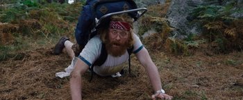 Movie still from “Cocaine Bear” (2023), directed by Elizabeth Banks – A man with a beard is laying on the ground with a backpack on his back; Medium shot, High angle