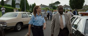 Movie still from “Cocaine Bear” (2023), directed by Elizabeth Banks – A police officer walking down a street with a man in a suit; Medium shot, Over the shoulder angle