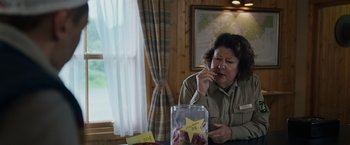 Movie still from “Cocaine Bear” (2023), directed by Elizabeth Banks – A woman sitting in front of a bag of apples; Medium shot, Over the shoulder angle