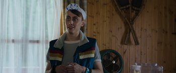 Movie still from “Cocaine Bear” (2023), directed by Elizabeth Banks – A young man wearing a hat and holding a cell phone in his hands; Medium shot, Over the shoulder angle