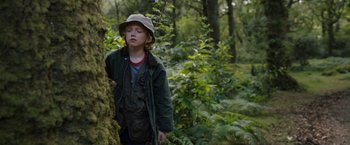 Movie still from “Cocaine Bear” (2023), directed by Elizabeth Banks – A young boy in a hat standing next to a tree in the woods; Medium shot, Low angle