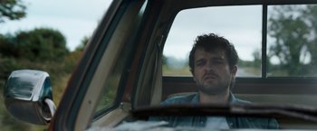 Movie still from “Cocaine Bear” (2023), directed by Elizabeth Banks – A man sitting in the driver's seat of a car; Close Up shot, Low angle