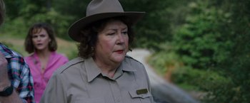 Movie still from “Cocaine Bear” (2023), directed by Elizabeth Banks – An older woman wearing a hat and a uniform; Close Up shot, Over the shoulder angle