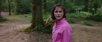 Movie still from “Cocaine Bear” (2023), directed by Elizabeth Banks – A woman wearing a pink shirt standing in front of a tree; Close Up shot, Over the shoulder angle