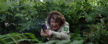 Movie still from “Cocaine Bear” (2023), directed by Elizabeth Banks – A woman holding a gun in her hands; Medium shot, Over the shoulder angle