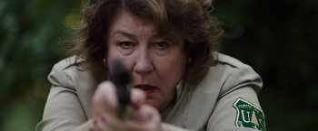 Movie still from “Cocaine Bear” (2023), directed by Elizabeth Banks – An older woman holding a gun pointed at the camera; Close Up shot, Low angle