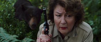 Movie still from “Cocaine Bear” (2023), directed by Elizabeth Banks – A woman holding a gun with a dog in the background; Close Up shot, Low angle