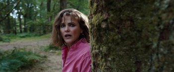 Movie still from “Cocaine Bear” (2023), directed by Elizabeth Banks – A woman wearing a pink jacket standing next to a tree; Close Up shot, Over the shoulder angle
