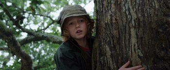 Movie still from “Cocaine Bear” (2023), directed by Elizabeth Banks – A young boy leaning up against a tree trunk; Close Up shot, Low angle