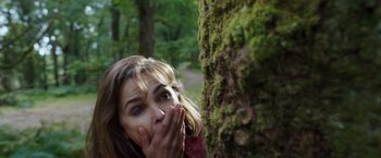 Movie still from “Cocaine Bear” (2023), directed by Elizabeth Banks – A woman covering her mouth near a tree trunk; Close Up shot, Low angle