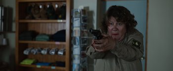 Movie still from “Cocaine Bear” (2023), directed by Elizabeth Banks – An older woman holding a gun in a room; Close Up shot, Over the shoulder angle