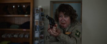 Movie still from “Cocaine Bear” (2023), directed by Elizabeth Banks – An older woman holding a gun in a room; Close Up shot, Over the shoulder angle