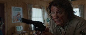 Movie still from “Cocaine Bear” (2023), directed by Elizabeth Banks – A person with a gun in a room with a window in the background; Close Up shot, Over the shoulder angle