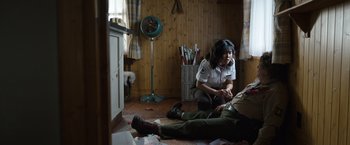 Movie still from “Cocaine Bear” (2023), directed by Elizabeth Banks – A police officer sitting on the ground talking to a man lying on the floor; Medium shot, High angle
