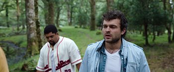 Movie still from “Cocaine Bear” (2023), directed by Elizabeth Banks – Two men are standing in a wooded area; Medium shot, Over the shoulder angle