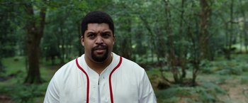 Movie still from “Cocaine Bear” (2023), directed by Elizabeth Banks – A man in a baseball uniform standing next to a forest; Medium shot, Low angle