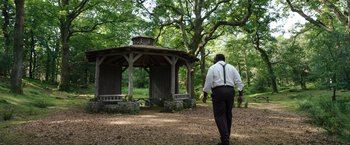 Movie still from “Cocaine Bear” (2023), directed by Elizabeth Banks – A man walking in the woods next to a gazebo; Extreme Wide shot, Over the shoulder angle